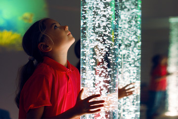 Child in therapy sensory stimulating room, snoezelen. Child interacting with colored lights bubble tube lamp during therapy session.