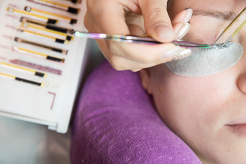 Beauty and fashion concept - Eye lash extension procedure. Young beautiful woman eye with long false eyelashes. Close up macro shot of fashion eyes in beauty salon.