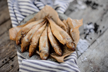 Delicious smoke-dried fish on plate on a baking paper on the grey striped napkin
