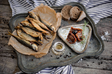 Smoke-dried horse mackerel fish on the paper on the metal tray with a sun dried tomatoes, oil and...