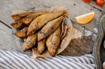 Smoke-dried fish on plate on a baking paper on the grey striped napkin with a salt and lemon