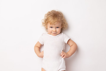 Caucasian curly baby girl in a white T-shirt on a white background hands holding a waist. child...