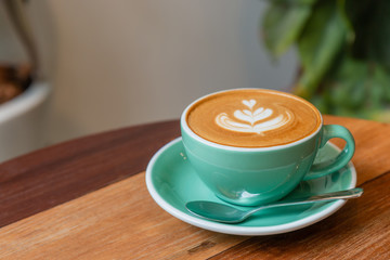 Hot cappuccino coffee in a green cup with latte art on the wooden table in the coffee shop.