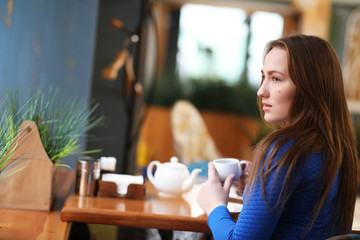 Young girl in cafe sits and drinks tea