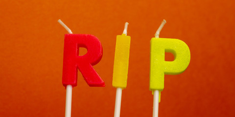 Banner horisontal concept word RIP from festive multi-colored wax paraffin candles on orange...