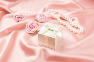 Obraz na płótnie Canvas Gift festive box with silk ribbon and flowers on a gentle pink satin background. Festive concept.