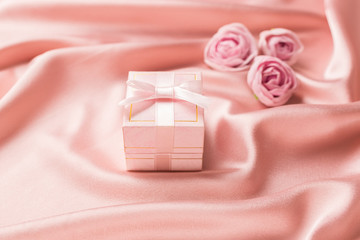 Gift box with silk ribbon and flowers on a gentle pink satin background. Festive concept.