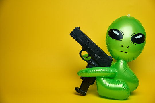 green alien looks,yellow background, green alien with gun