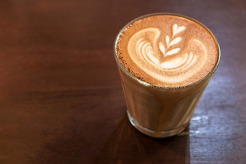 Coffee glass cup on a saucer of morning fragrant cappuccino with foam on a wooden table, place for an inscription