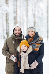 Waist up portrait of happy modern family in winter forest posing with little girl and smiling at...