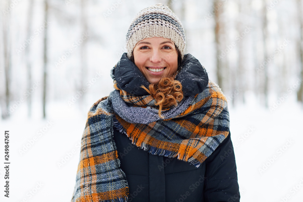 Wall mural waist up portrait of beautiful young woman in winter forest looking at camera and smiling, copy spac