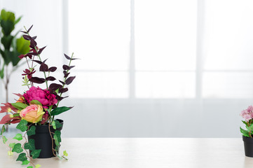 There are beautiful flowers and various objects in front of big living room windows.