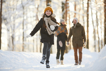 Full length portrait of happy little girl running towards camera in winter forest while enjoying...