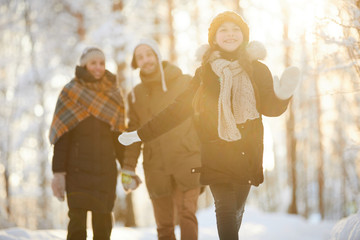 Portrait of happy little girl running towards camera in winter forest lit by sunlight while enjoying walk with family, copy space