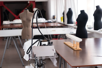 Tables for cutting fabric in the sewing workshop on the background of mannequins and steam iron - obrazy, fototapety, plakaty