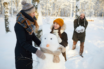Portrait of happy family building snowman in winter forest and having fun, copy space