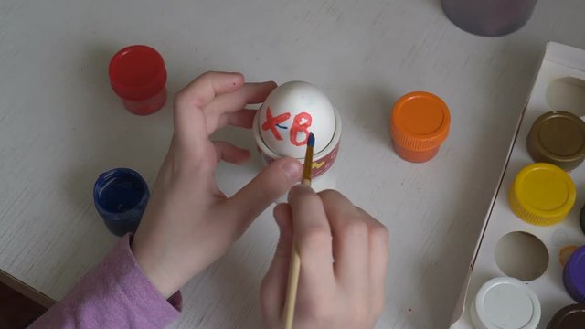 The child paints Easter egg colors and draws symbols on it with a brush. Close up. The view from the top. 4K. 25 fps