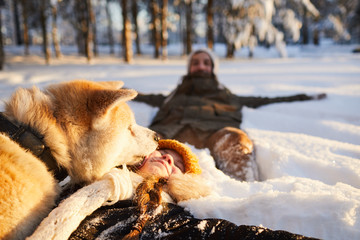 Portrait of happy little girl playing with dog in beautiful winter forest, copy space