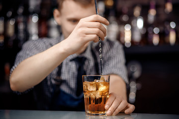 Barman shakes cocktail with ice in glass long spoon