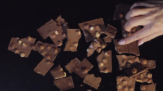 Woman hand takes one piece of chocolate bar from a bunch of chocolate pieces. Slow motion