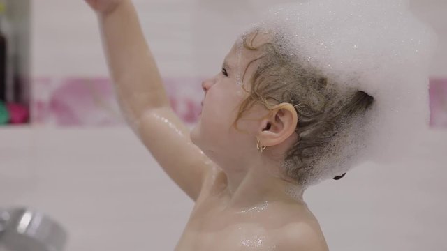 Attractive three years old girl  takes a bath. Mom clean hair with a shampoo. Cute blonde child. Brown eyes. Girl does not like to wash her hair. Pretty little child, 3-4 year old blonde girl