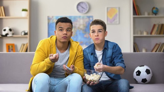 Anxious teenage friends watching football match on TV and eating popcorn leisure