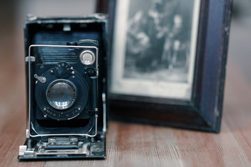 Close up image of old vintage dusty camera with old picture on blurred background, selective focus. Wooden table, indoors, retro effect, copy space.