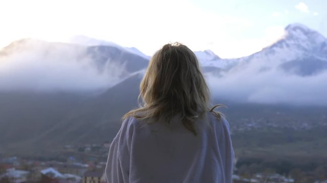 woman in bathrobe stands with his back and looks at the mountains