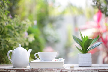 White coffee cup and kettle with notebooks on wooden table with green plants