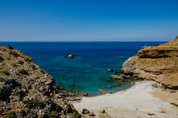 Fototapeta na wymiar Secluded beach with clear blue water and small pebbles and sand, away from mass tourism in village of Chora Sfakion. Crete, Greece.