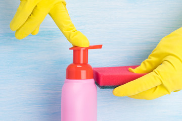 hands in rubber yellow gloves pour dishwashing liquid on a sponge on a light background