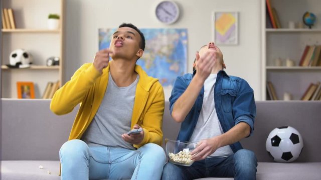 Multiracial male teen friends discussing football match eating popcorn, leisure