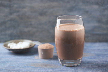 Glass of Chocolate Protein Shake with milk and banana. Whey protein in scoop and BCAA amino acids in background. Sport nutrition.Wooden background. Copy space. 