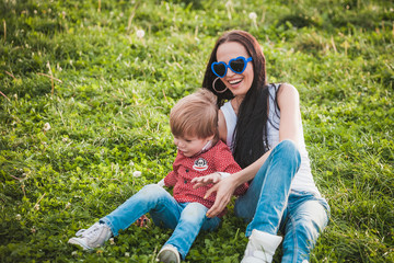 happy mother with her little son sitting on grass in summer day