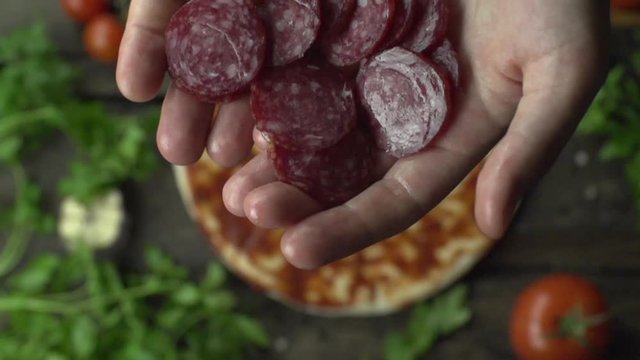 Cook throws pepperoni on pizza slow motion