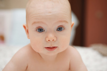 Beautiful five-month blue-eyed baby baby girl lying on her stomach, various emotions and smile on her face. Infant look. Maternal care. Childcare. Close-up.