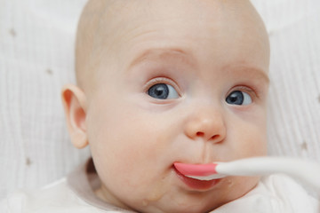 Beautiful Lovely five-month baby girl eating with a spoon. Healthy food. Maternal care. Childcare. Close-up.