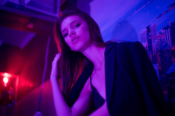 Fashion portrait of young elegant girl. Beautiful brunette woman in neon light. Underwear, jacket shows a bare tummy. Colored background, studio shot