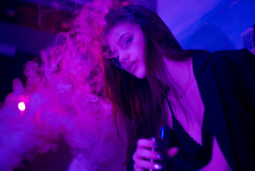 Obraz na płótnie Canvas Portrait of glamour seductive gorgeous brunette woman smoking electronic cigarette in neon color light in studio