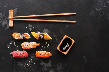 Assorted sushi set on a black stone background. Japanese food sushi, soy sauce, chopsticks. Top view, copy space.