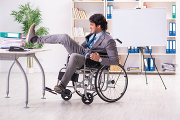 Fototapeta na wymiar Young handsome employee in wheelchair at the office 
