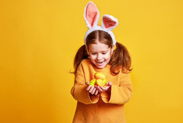 funny happy child girl with easter eggs and bunny ears on yellow