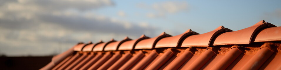 glänzend rote Dachziegel Pfanne vom Dachdecker Handwerker im Sonnenschein vor dunklem Hintergrund