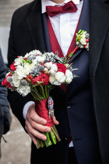 Groom holding a winter wedding bouquet with a brooch