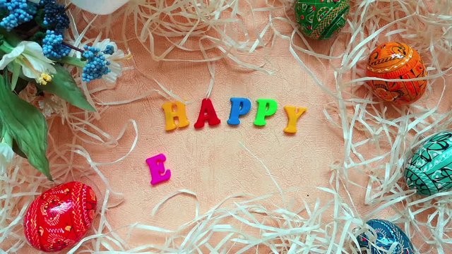 Woman puts colourful words Happy Easter on table decorated with easter eggs and decorative straw. Top view