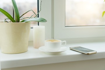 Abstract photo windowsill morning white cup with coffee mobile phone, nobody home interior