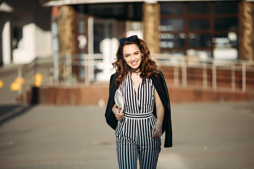 Fototapeta premium Beautiful smiling woman wearing in striped dress, leather jacket, choker,with handbag, posing, walking at street. Brunette girl in stylish spring look with make up,haircut, sunburn after beauty salon.