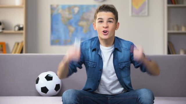 Excited teenage student watching football match on TV cheering for national team