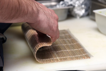 Close-up of a cook preparing sushi rolls in the kitchen of restaurant, wrapped in a bamboo mat. The concept of cooking Japanese dishes