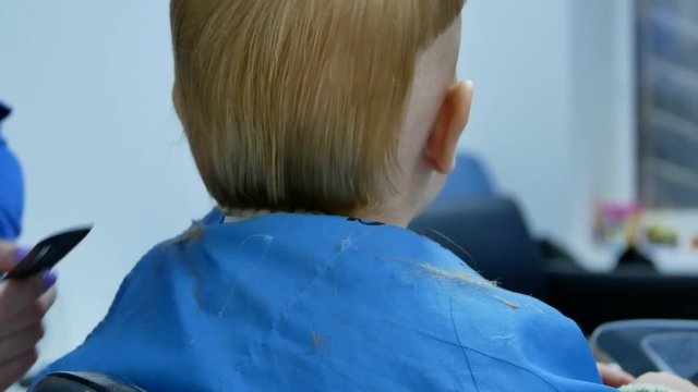 hairdresser trying to cut off hair with scissors from backhead cute 2 years old little boy while he spin his head. view from back close up 4k video footage